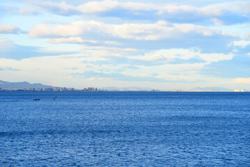 Sea with waves against the backdrop of mountains and buildings and houses. Seascape of Mediterranean Sea. View on Coastline in La Pobla de Farnals (Puebla de Farnals) in Valencia. Rock mountain at sea
