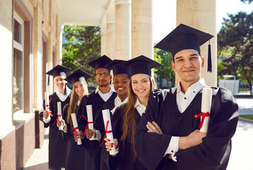 Group portrait of happy graduates in campus yard. Six international students in caps and gowns...