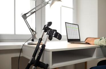 Crutches close-up on the background of workplace with laptop during remote work. Recovery at home after physical injuries. Young man sits at desk in the living room and works from home.