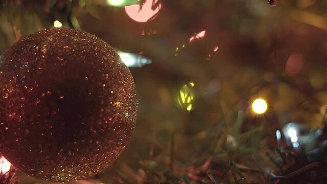Sparkling Christmas ornament ball hanging on tree rotating while lights flash in background
