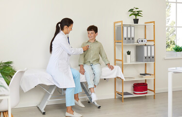 Child getting health checkup in exam room at doctor's office. Pediatrician sitting on medical couch...