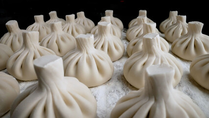 A pile of homemade raw khinkali dumplings close-up on the table. Khinkali before cooking, hand-baked. Georgian Khinkali in Flour Before Cooking. Khinkali before cooking.