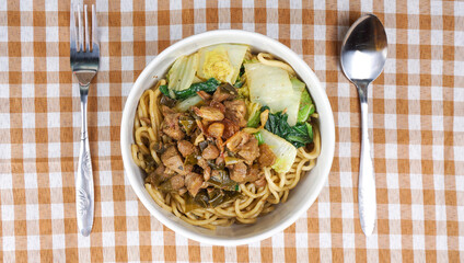 Top view of Mie Ayam as Indonesia chicken noodles topped with diced chicken, green vegetables and chili sauce in white background