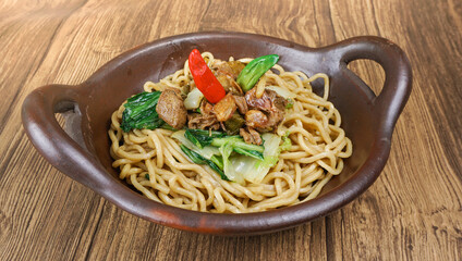 Plate of noodles with chicken and vegetables on wooden table.