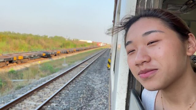 Happy young beautiful asian woman enjoy train ride cinematic nature view blue sky slow motion holding cellphone in hand taking picture. Tourism and holiday concept, Thailand