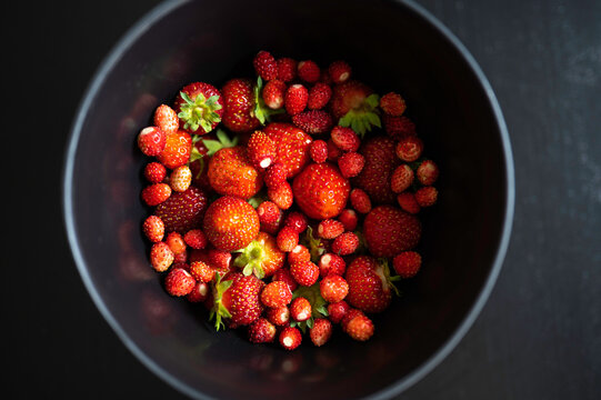 Closeup of strawberries and wild strawberries in a black bowl on a black table. Finland