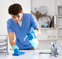 Portrait of professional worker of office cleaning service wiping furniture with rag and detergent