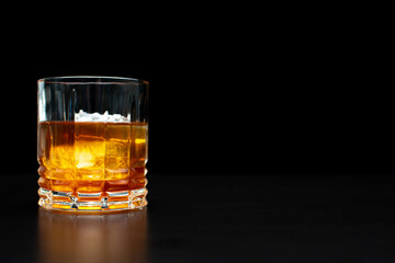 glass with orange yellow liquor with ice on a black background reflection of the glass on the table with space for text