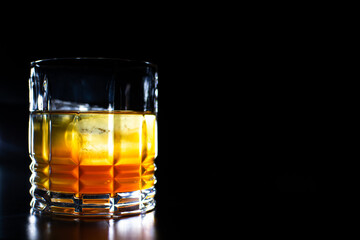 
glass with orange yellow liquor on a black background reflection of the glass on the table