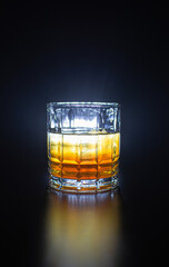 
glass with orange yellow liquor on a black background reflection of the glass on the table