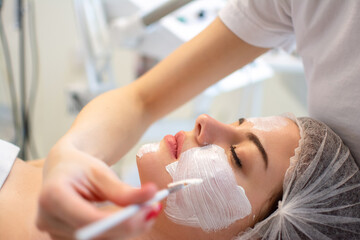 Obraz na płótnie Canvas Face peeling mask, spa beauty treatment, skincare. Beautician applying peeling mask to woman at spa salon, side view, close-up.
