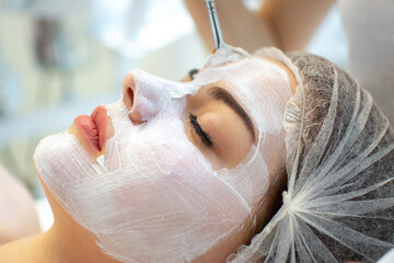 Face peeling mask, spa beauty treatment, skincare. Woman getting facial care by beautician at spa salon, side view, close-up.