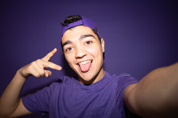Smiling teenager boy posing and taking selfie isolated on purple background