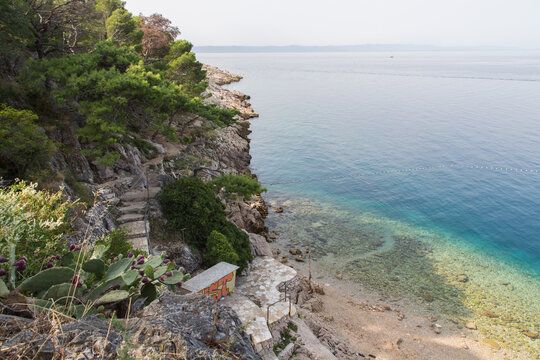 Way downstairs to a pretty pebbly  beach with shady pine trees near Makarska village at the beautiful coastline called Makarska Riviera, Croatia with crystal clear and turquoise water.