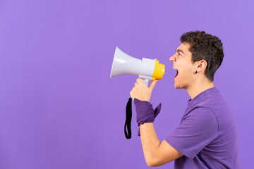 Feminist protestor young man shouting on megaphone isolated on purple background with copy space.