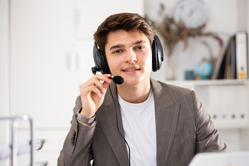 Positive businessman with headphones and microphone having video call on laptop in modern office