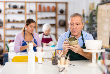 Satisfied mature man demonstrates pottery made by her own hands