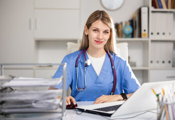 Young woman doctor sitting at table in her office and looking at camera.