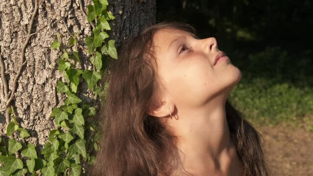 Eco child stay by tree trunk. An eco friendly little girl relax by the tree trunk in the sunny park. A concept of healthy and ecological life style.