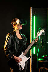 Woman performer playing at electric guitar in sound studio while wearing vr goggles for concert...