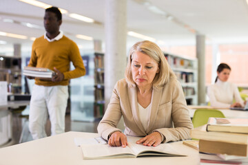 Fototapeta premium Woman with books sits at table in the library. High quality photo