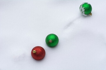 Red and green Christmas ornaments in snow during winter storm