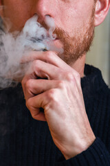 Close up of man smoking a vape device breathing out vape cloud