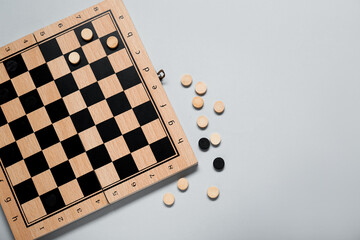 Wooden checkerboard and game pieces on light grey background, flat lay. Space for text