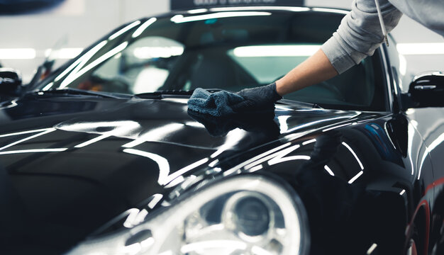 Man using a microfiber cloth to apply ceramic coating onto a shiny expensive black car. Unrecognizable person in protective gloves. High quality photo