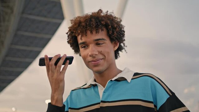 Modern guy listening mobile voice message at street. Curly hipster holding phone