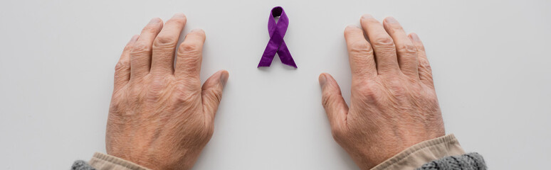 top view of cropped male hands near purple alzheimer disease awareness ribbon on white surface,...