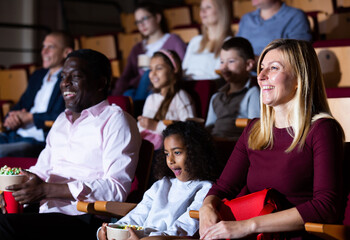 Fototapeta na wymiar Portrait of laughing european woman watching funny movie in cinema with her african husband and preteen daughter