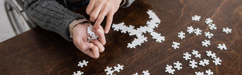 cropped view of man with parkinson syndrome and tremor in hands holding elements of jigsaw puzzle,...