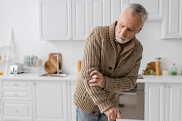 grey haired man suffering from parkinsonism and hands tremor standing with walking cane in kitchen...