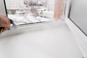 Fototapeta na wymiar Steam cleaning of window frame at home. Professional cleaner is disinfecting window frame. Professional cleaning service cleans dirt and dust on balcony at home.