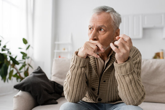 depressed and anxious man with parkinson disease holding trembling hands near face and looking away at home.