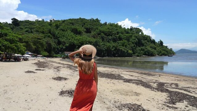 Summer beach vacation. Young woman with hat relaxing enjoying walking on the beach ocean on hot summer day in Brazil.