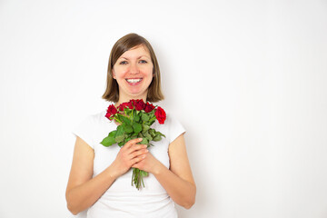 Portrait of happy smiling girl in white shirt with bouquet of red roses in hands. 