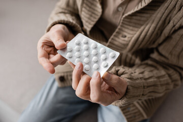 partial view of aged man with parkinsonian syndrome holding pills in trembling hands.