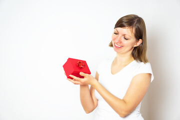 Happy pretty young woman in a white shirt holding a red gift box on the white background.