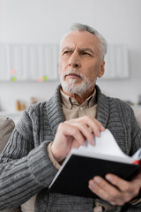 Fototapeta premium pensive man suffering from memory loss while holding blurred notebook and looking away at home.