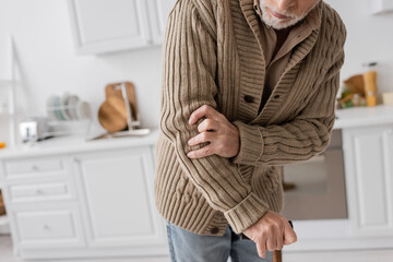 partial view of senior man with parkinson disease and hands tremor standing with walking cane in...