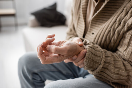 partial view of senior man with parkinsonism holding trembling hand while sitting at home.