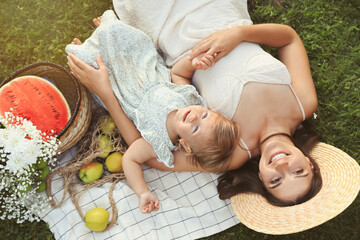 Mother and her baby daughter resting while having picnic on green grass outdoors, above view