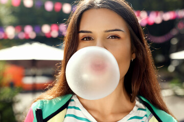 Beautiful young woman blowing chewing gum on city street outdoors
