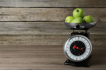 Kitchen scale with green apples on wooden table. Space for text