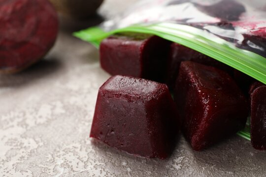 Frozen beet puree cubes in plastic bag on marble table, closeup