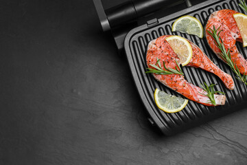 Cooking salmon. Grill with fresh fish steaks, lemon and rosemary on dark table, top view. Space for text