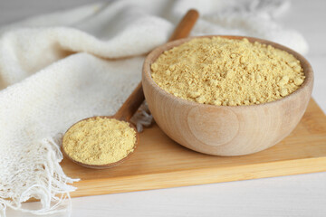 Bowl and spoon with aromatic mustard powder on white wooden table, closeup