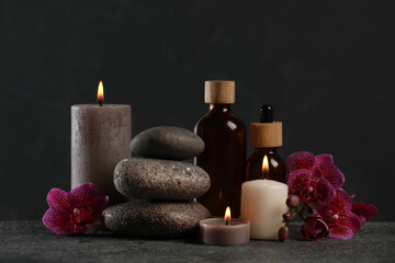 Fototapeta na wymiar Beautiful composition with burning candles, spa stones and different care products on dark grey table